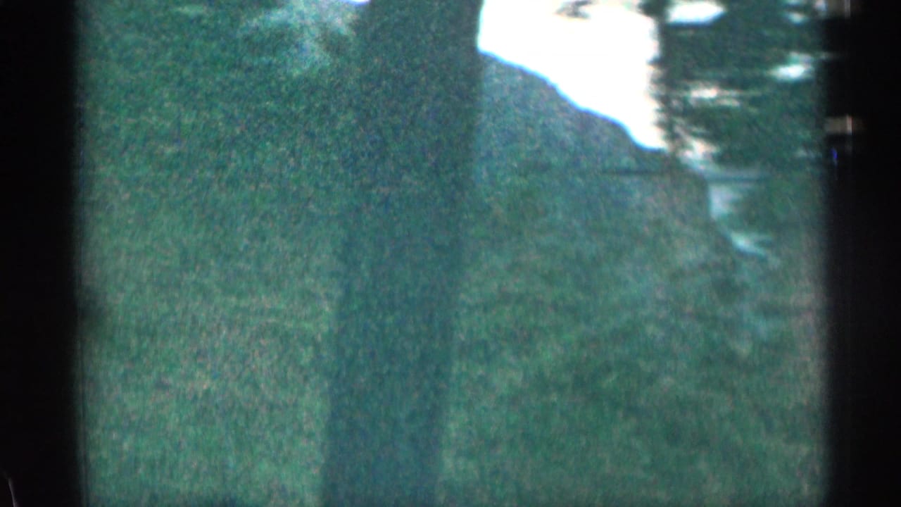 1963 Colorado 8mm frame showing green mountain slopes and distant peaks through dark vehicle or window framing.