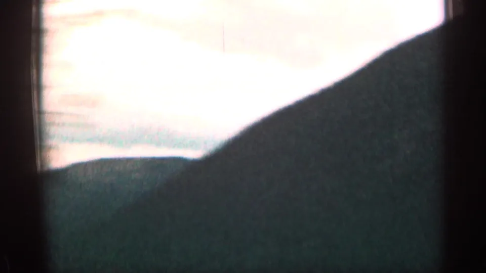 Brief 1963 Colorado road-trip frame with an overexposed sky and dark mountain or roadside silhouette.