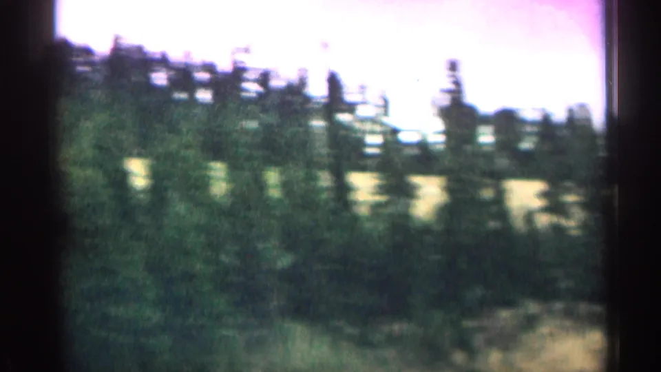1963 Colorado home-movie frame with blurred pine forest, pale slope, and bright sky from a moving car viewpoint.