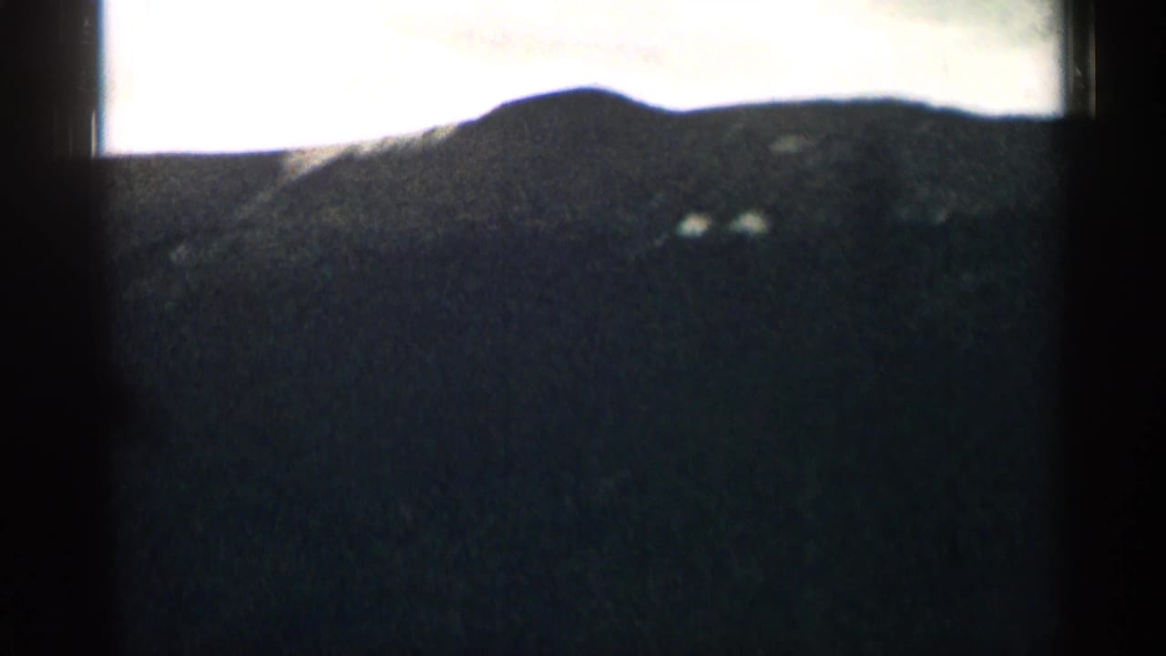 Dark mountain slope seen through a car window with a bright sky above.