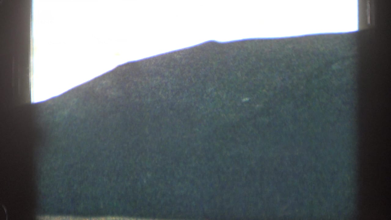Rounded mountain ridge seen through dark car-window framing under a bright sky.