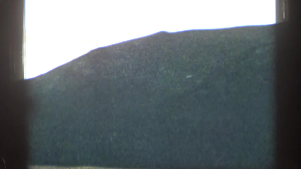 1963 Colorado road-trip frame showing a rounded mountain ridge through the interior window frame of a moving car.