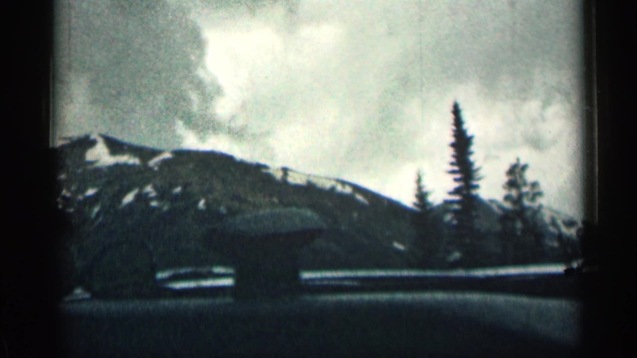 1963 Colorado home-movie frame showing snowy mountain slopes and evergreen trees seen through a car window during travel.