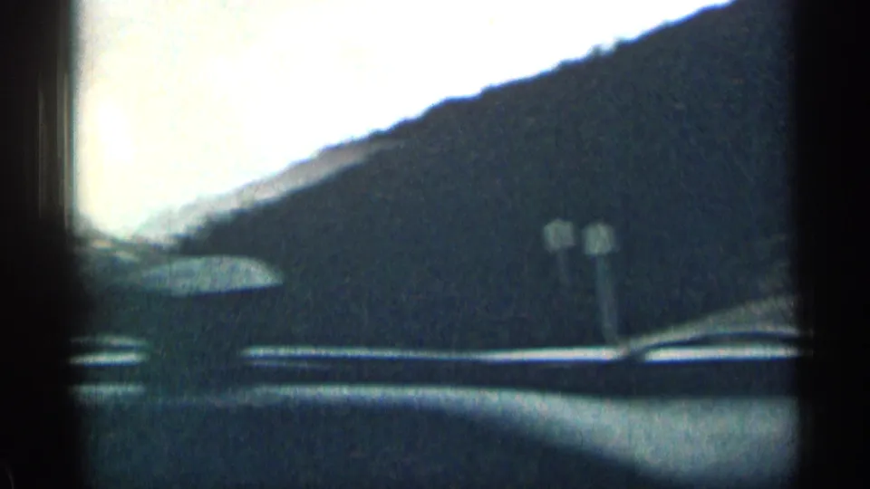 1963 Colorado driving view from inside a moving car, with dashboard lines and a mountain slope visible ahead.