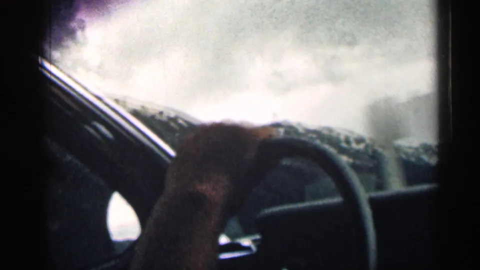 1963 Colorado home-movie view from the driver area, showing a hand on the steering wheel and snowy peaks through the windshield.