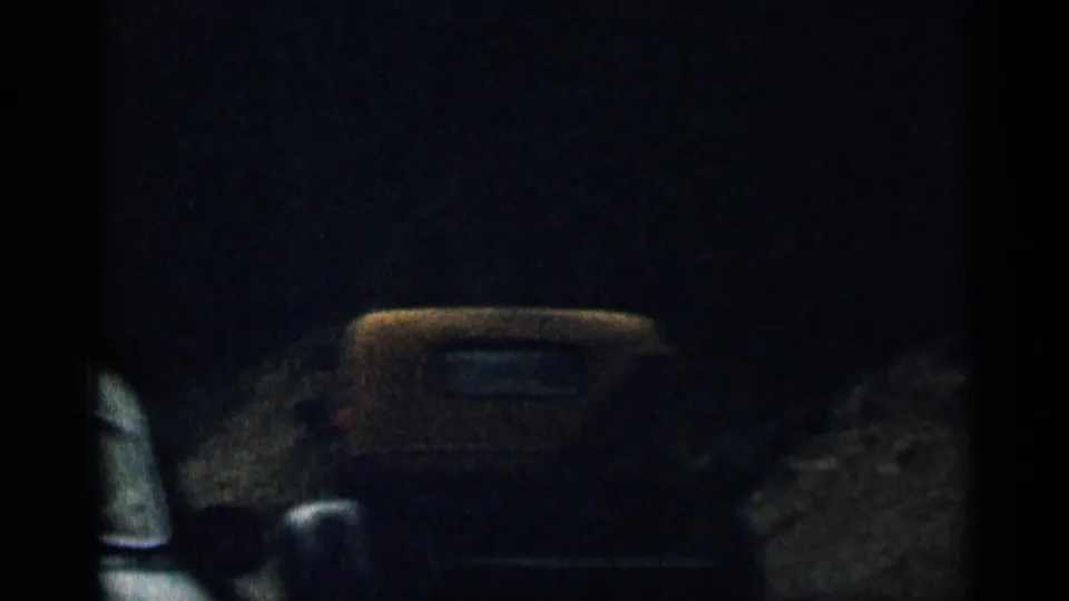 Dim 1963 Colorado 8mm road-trip frame showing shadowed vehicles or car bodies along a dark roadside view.