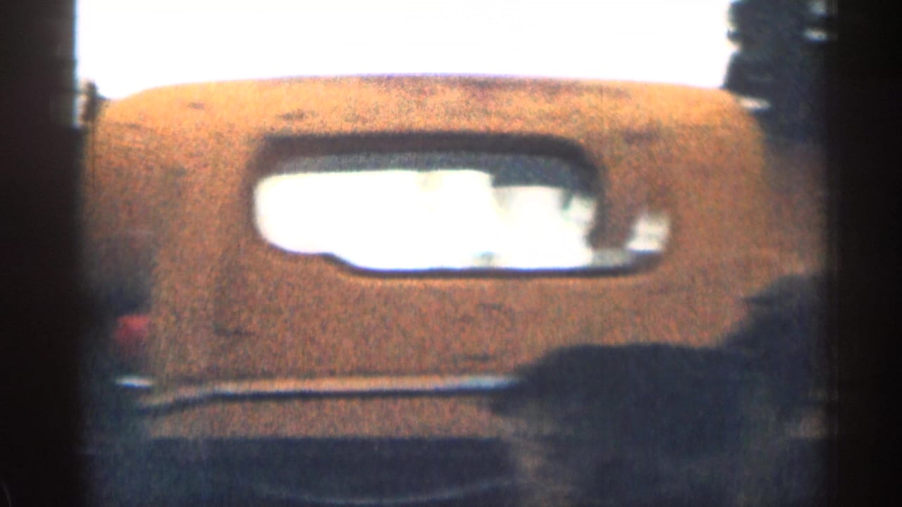 Brown dog visible in the back of a truck, framed against the rear cab window in grainy 1963 Colorado footage.