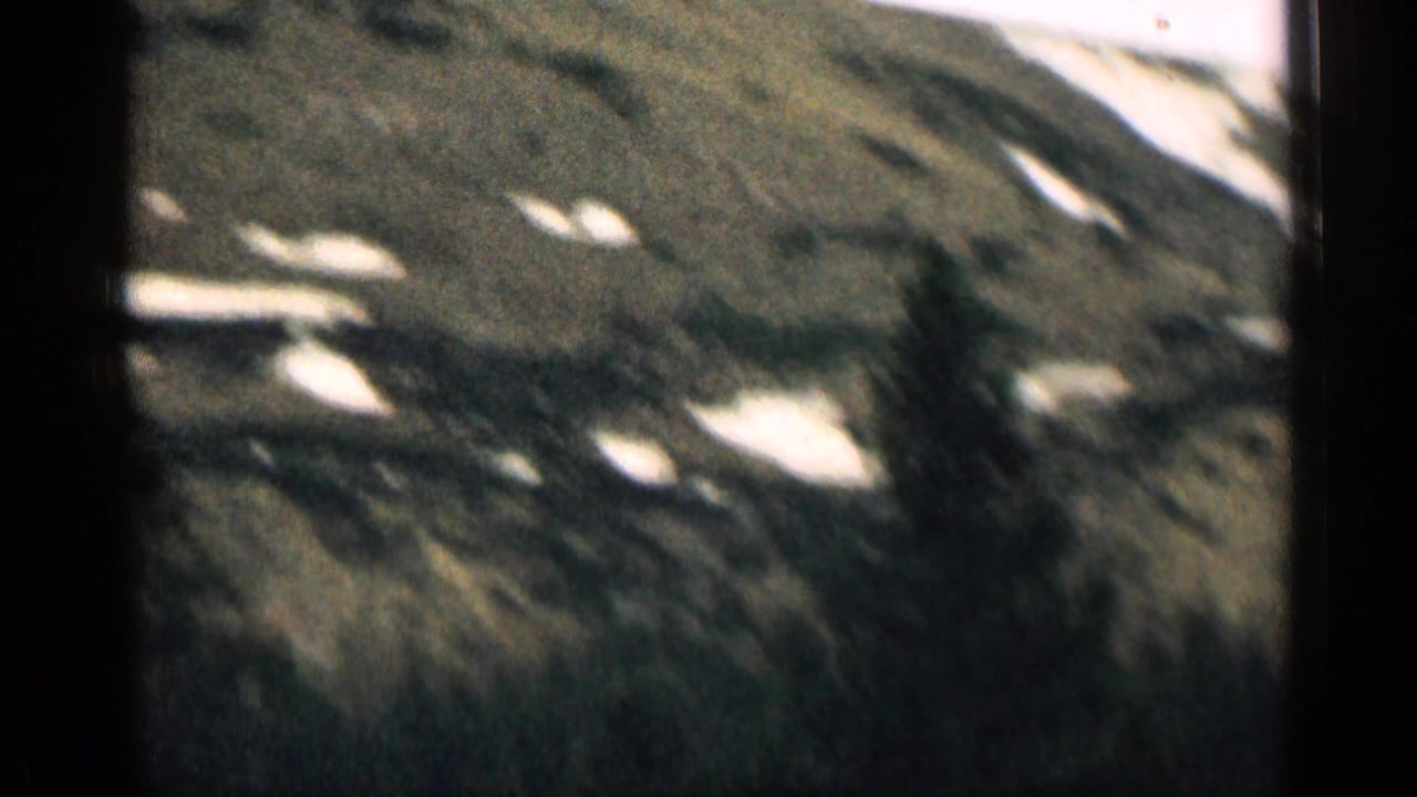 1963 Colorado home-movie frame showing a rugged mountainside with lingering snow patches and dark rocky terrain.