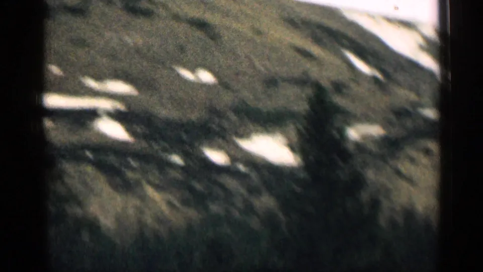 1963 Colorado home-movie frame showing a rugged mountainside with lingering snow patches and dark rocky terrain.