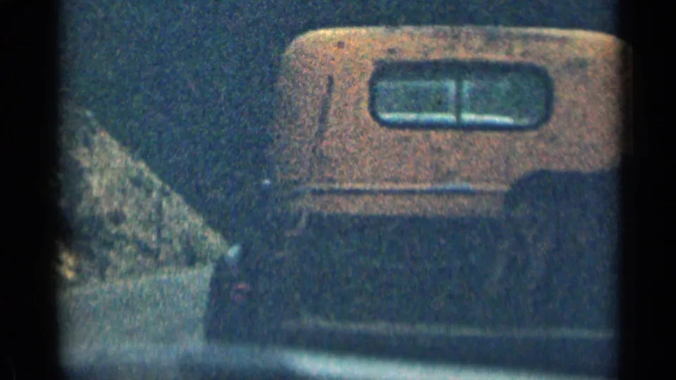 1963 Colorado 8mm frame showing the side of a boxy orange-and-dark vintage truck near rocky roadside terrain.