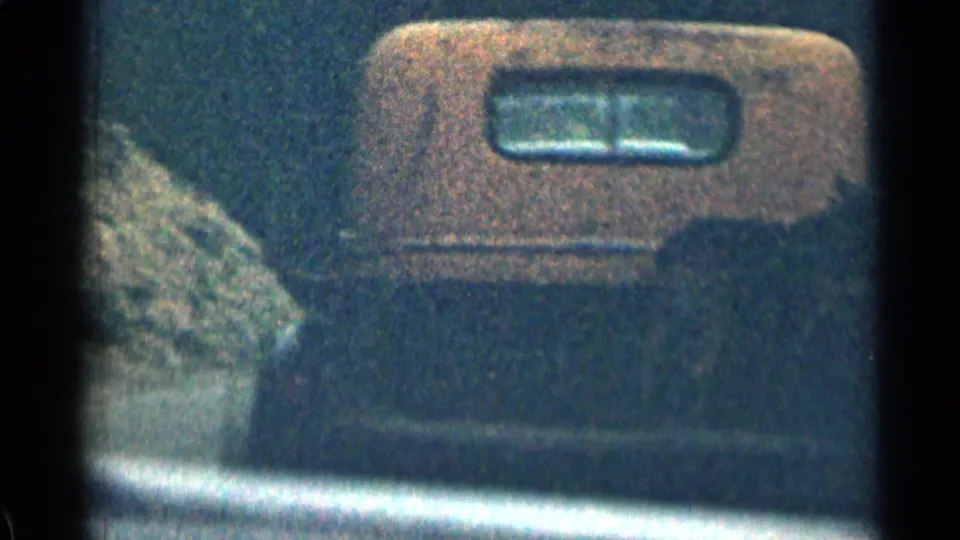 Boxy orange-and-dark truck seen from the side in 1963 Colorado mountain-road home-movie footage.