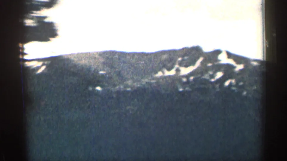 1963 Colorado 8mm view of a snow-patched mountain ridge, with dark foreground and strong overexposure in the sky.