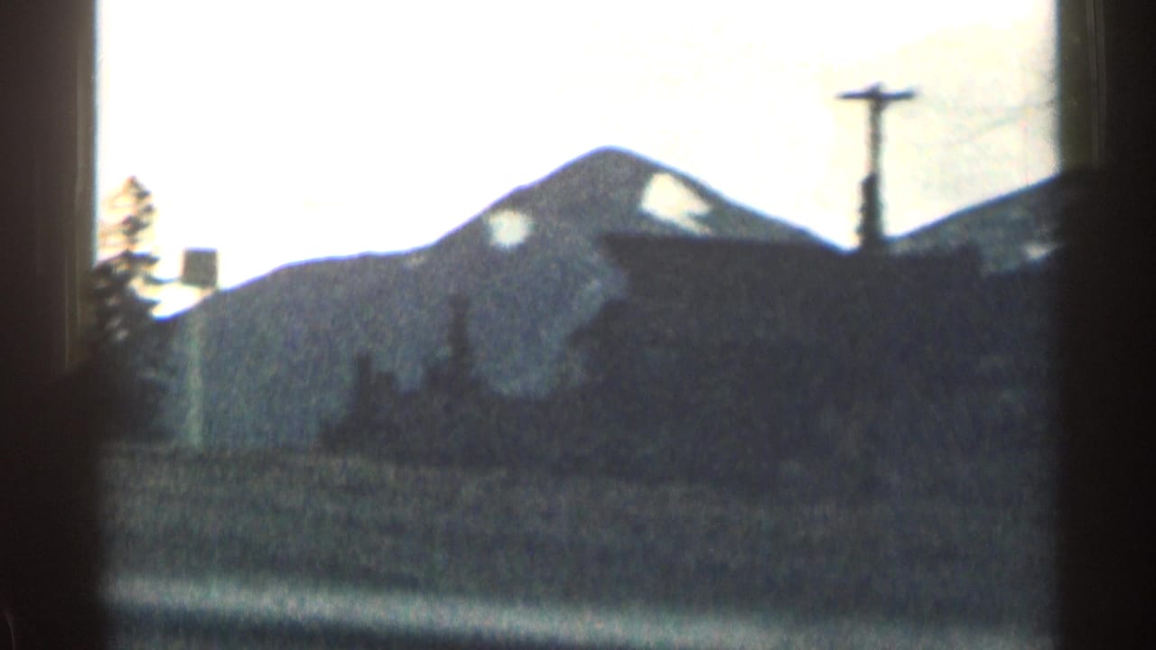 Dark mountain ridge with snow patches behind trees and a utility pole.