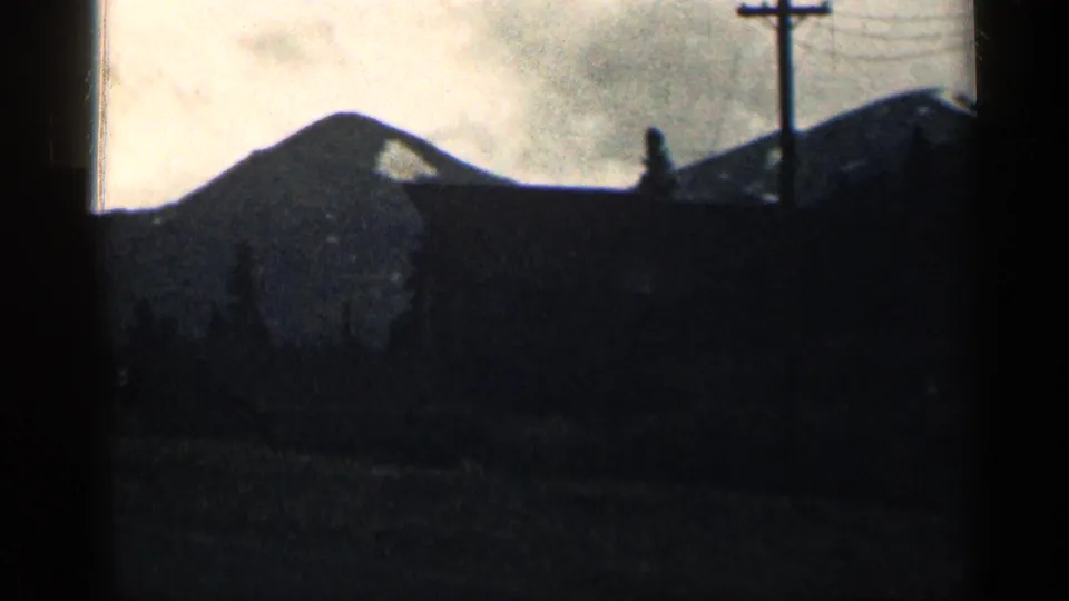 A shadowed building or roofline sits below a Colorado mountain ridge, with a utility pole silhouetted against the pale sky.
