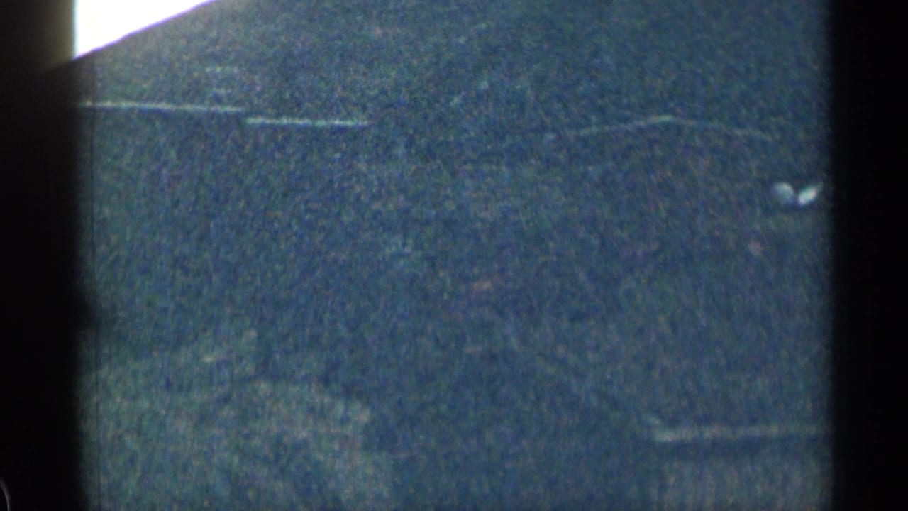 Low-light 1963 Colorado 8mm frame showing a dark textured exterior field with faint horizontal lines and heavy film grain.