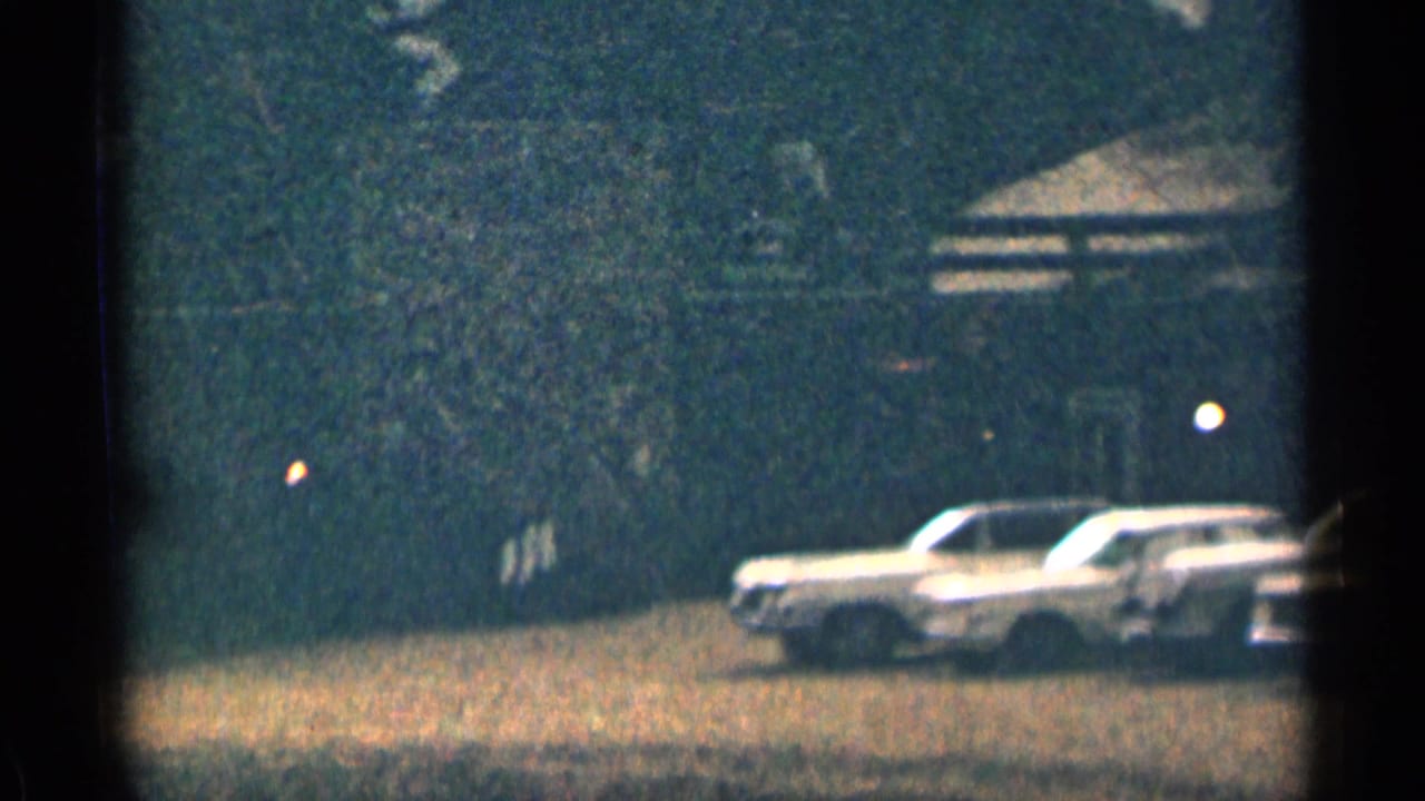 White sedan parked near trees and a low cabin roofline in a wooded mountain setting.