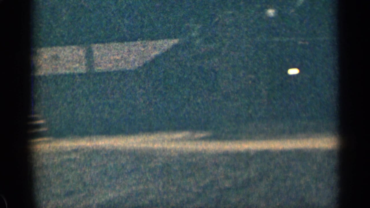 Dark wooded slope with a pale roofline and bright film flare at the edge of frame.