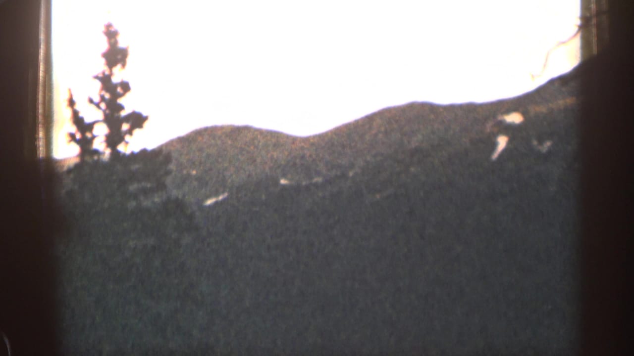 Sunlit mountain ridge and evergreen trees seen through dark film-frame borders.