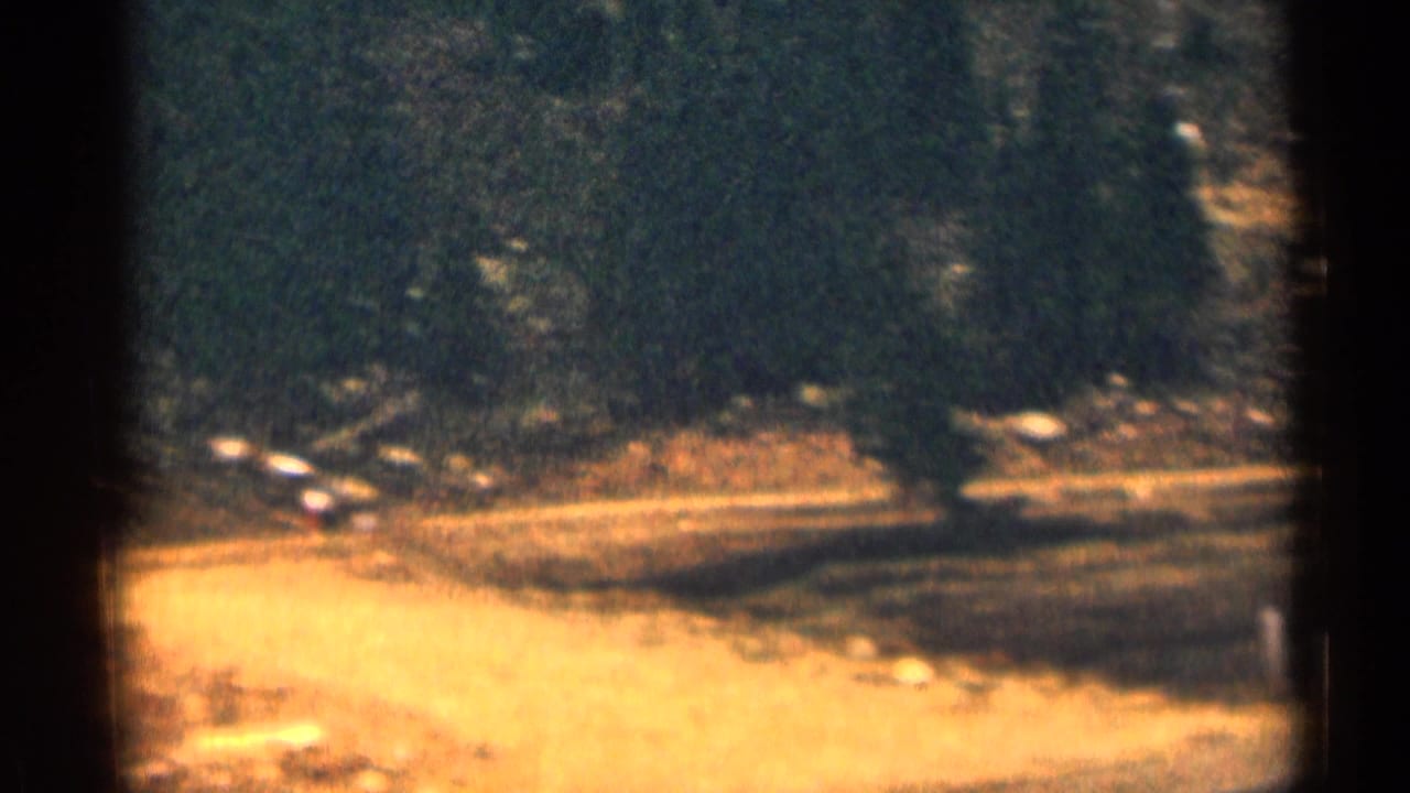 1963 Colorado home-movie frame with a 40 mph sign near a curving rural road and wooded dry terrain.