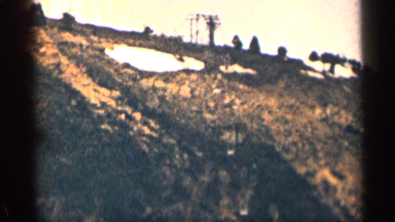1963 Colorado 8mm frame showing a bright hillside, rough ground, and small distant roadside structures.
