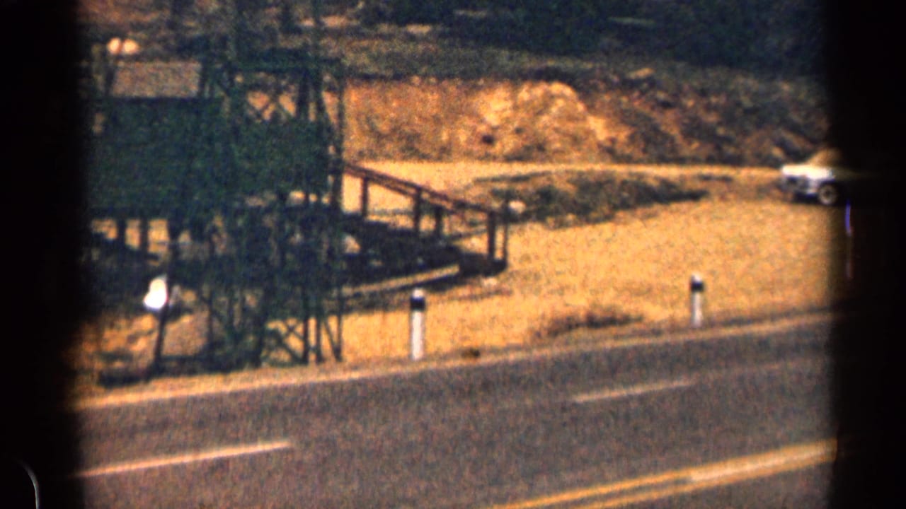1963 Colorado roadside view with wooden construction framing, a paved road edge, a small person, and a parked white car.
