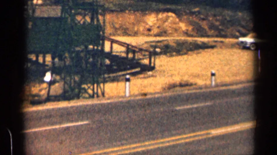 1963 Colorado 8mm view of a paved roadside, wooden construction framing, a small person, and a parked white car.