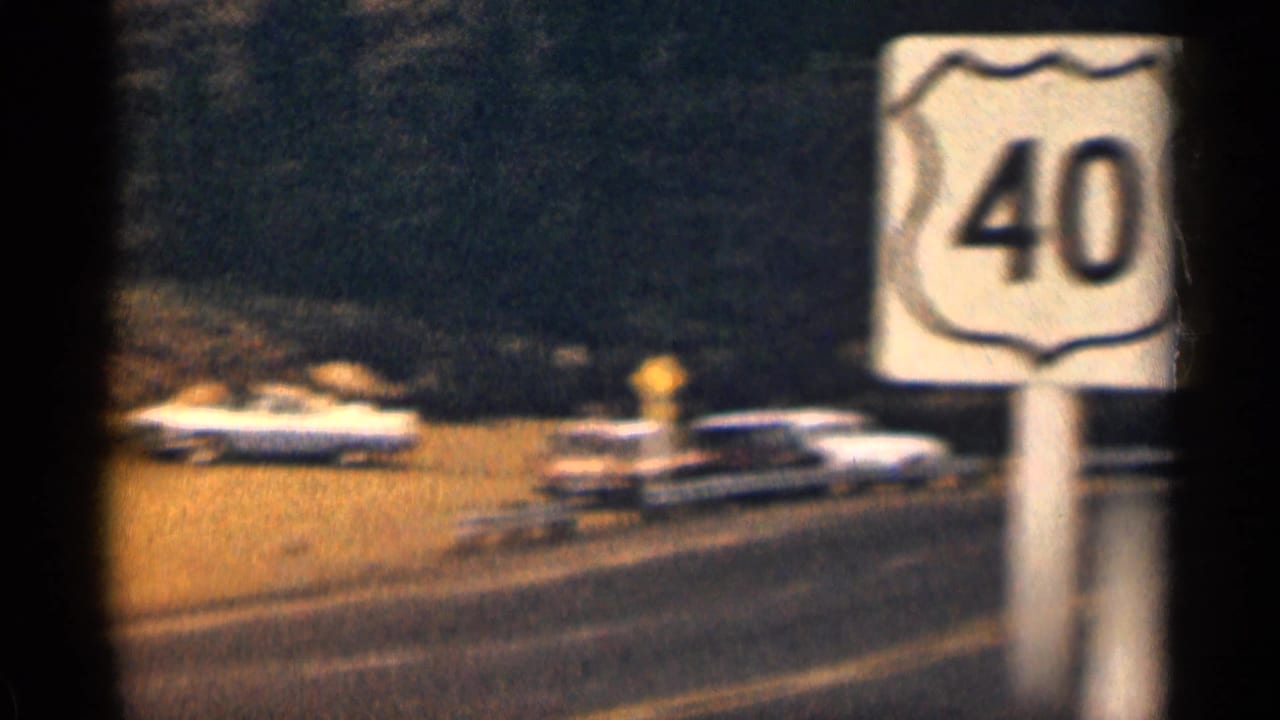 1963 Colorado home-movie frame showing a Route 40 shield near a quiet highway with passing mid-century cars.