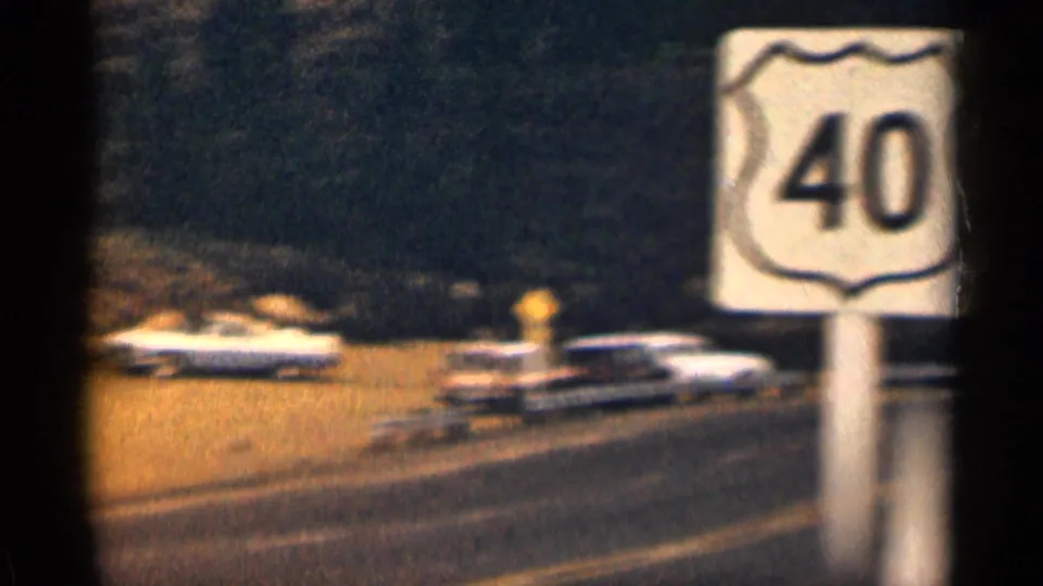 1963 Colorado home-movie frame showing a Route 40 shield near a quiet highway with passing mid-century cars.