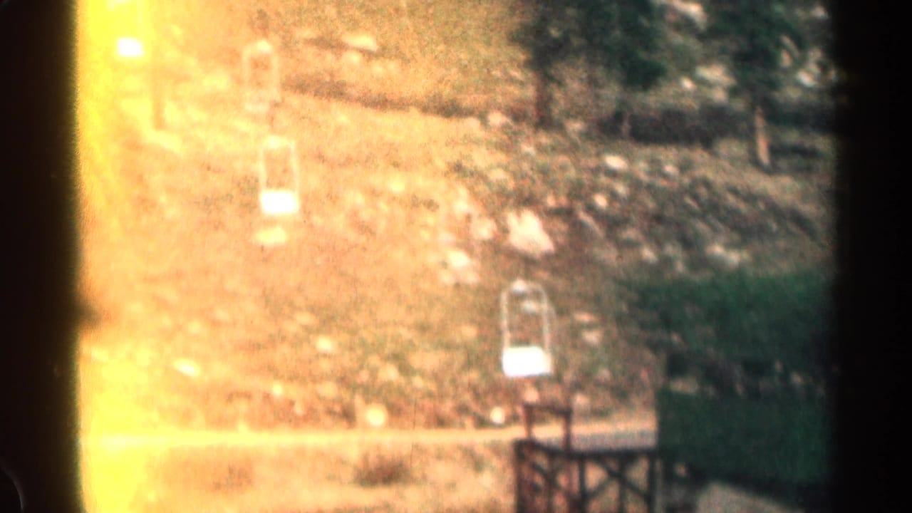 1963 Colorado 8mm frame showing an older car traveling on a mountain road below a rocky, tree-lined hillside.