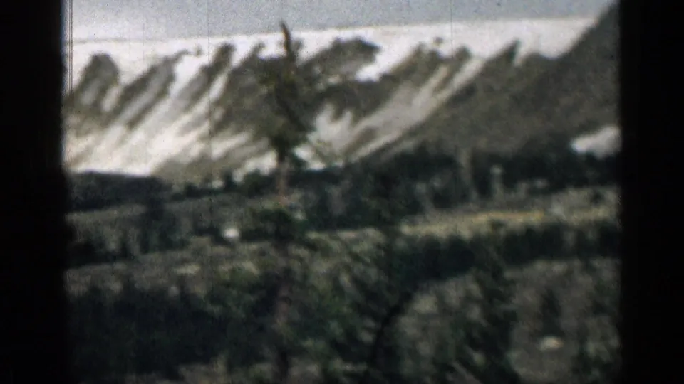 1963 Colorado home-movie view of snow-dusted mountains above dark evergreen forest, with heavy grain and soft focus.