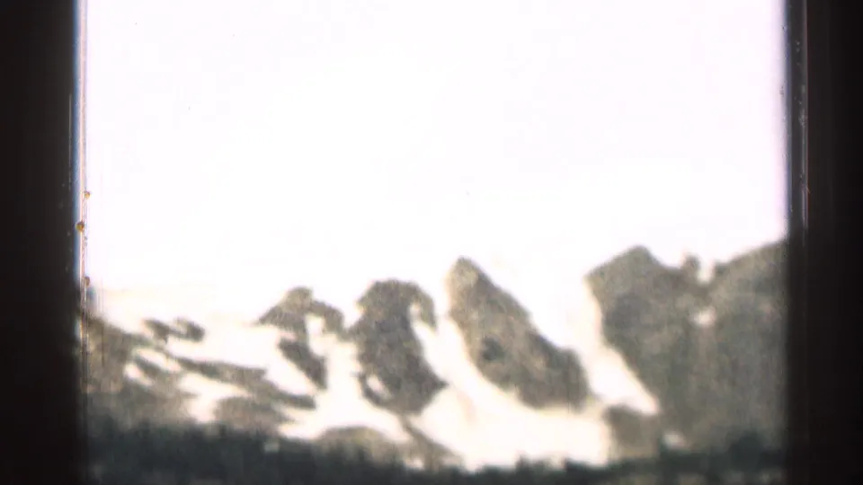 1963 Colorado 8mm frame showing snow-covered mountain peaks beneath a bright, overexposed sky.