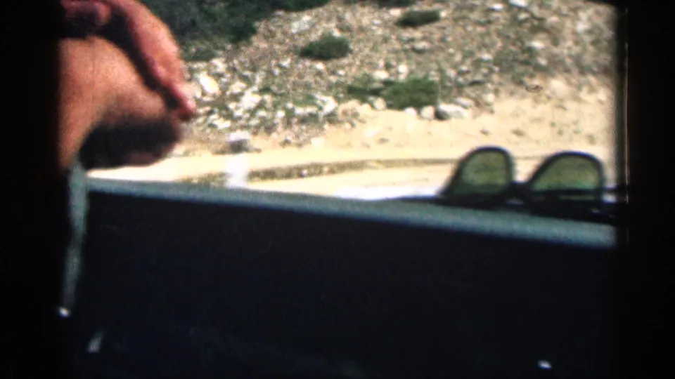 Interior car view during a Colorado drive, with part of an adult passenger, sunglasses on the dashboard, and a rocky hillside outside.