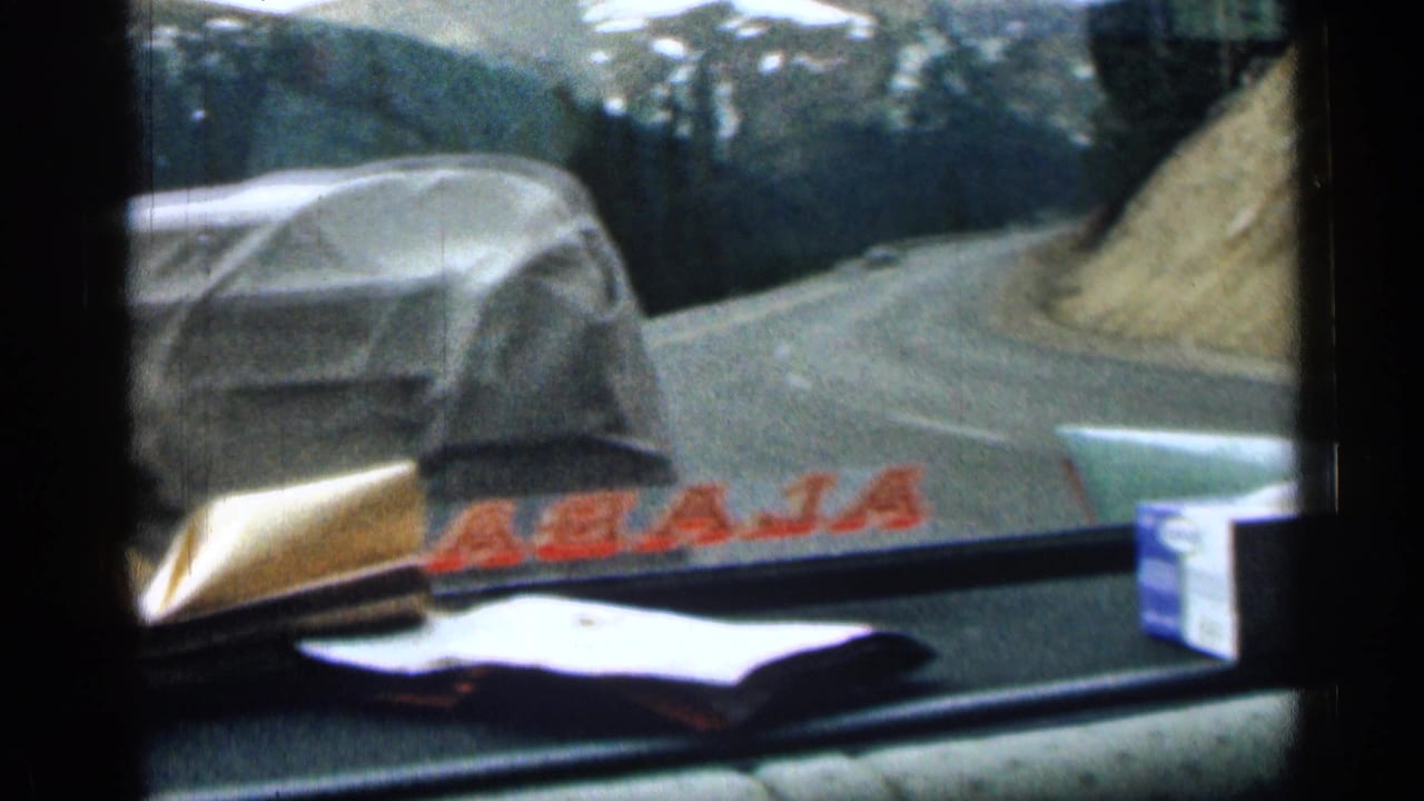 1963 Colorado 8mm frame from inside a car, showing dashboard items, a winding mountain road, and a covered car ahead.