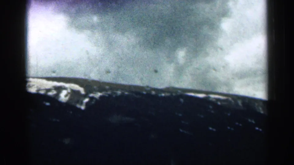 1963 Colorado 8mm frame showing a dark mountain ridge, scattered snow, and cloudy sky from a moving vehicle.