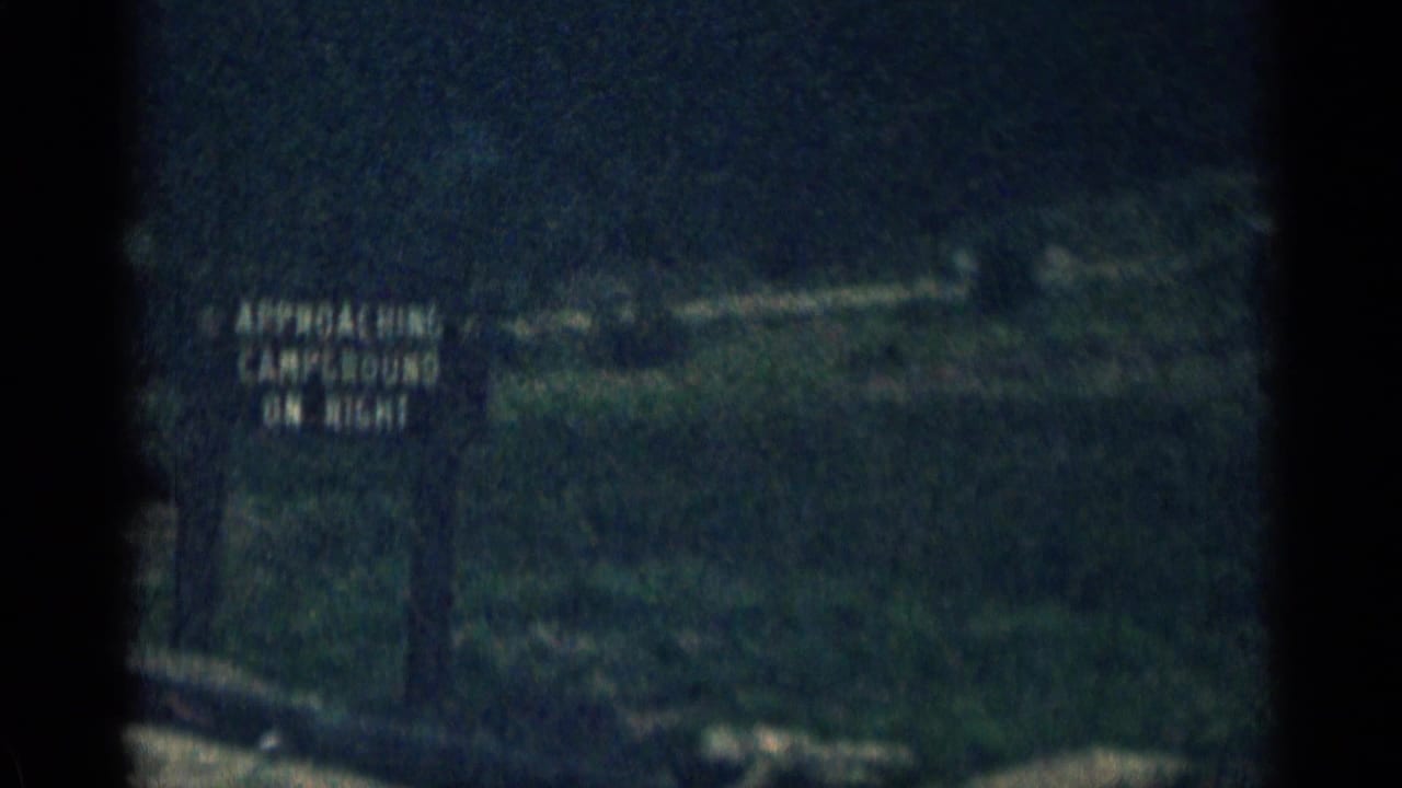 Roadside sign near a mountain road reads as an approaching campground notice.