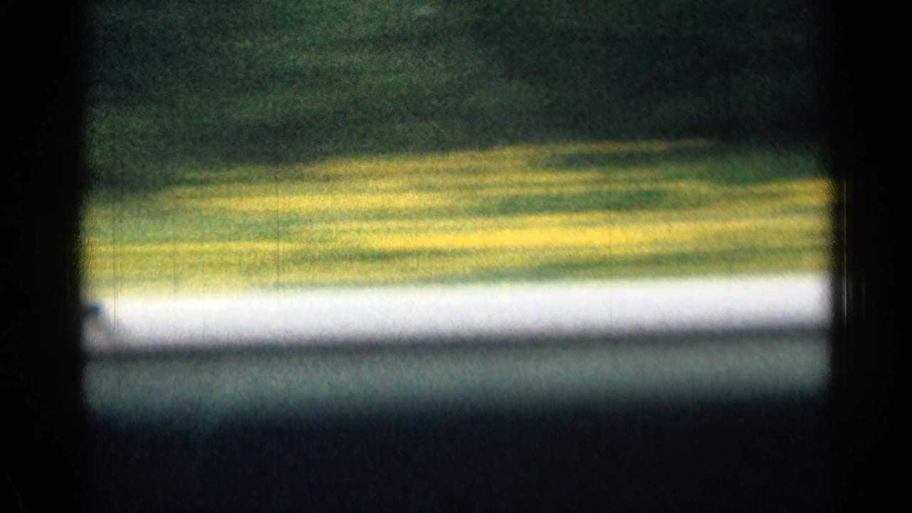 1963 Colorado road-trip frame showing blurred greenery and a white roadside barrier from inside a moving car.