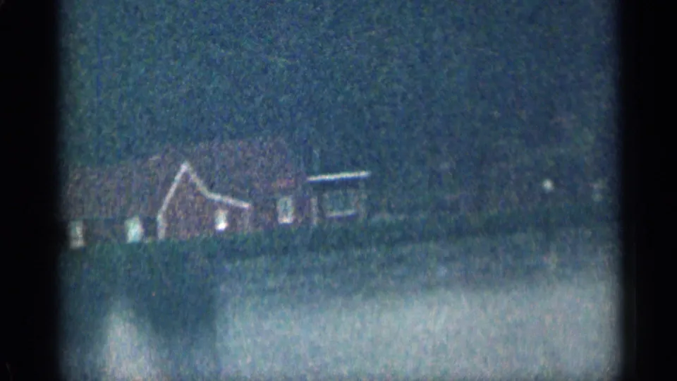 Distant house-like building among trees in the 1963 Colorado home-movie view, with soft focus and a pale foreground band.