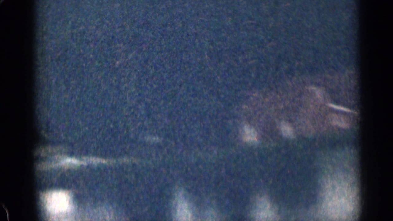 1963 Colorado 8mm frame showing a dark roadside or shoreline view with faint building lights and soft reflections below.