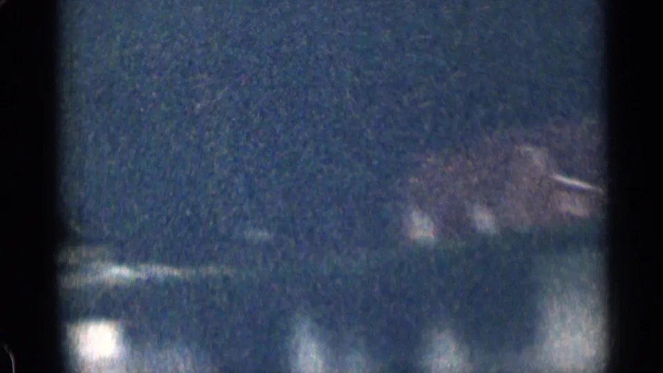 1963 Colorado 8mm frame showing a dark roadside or shoreline view with faint building lights and soft reflections below.