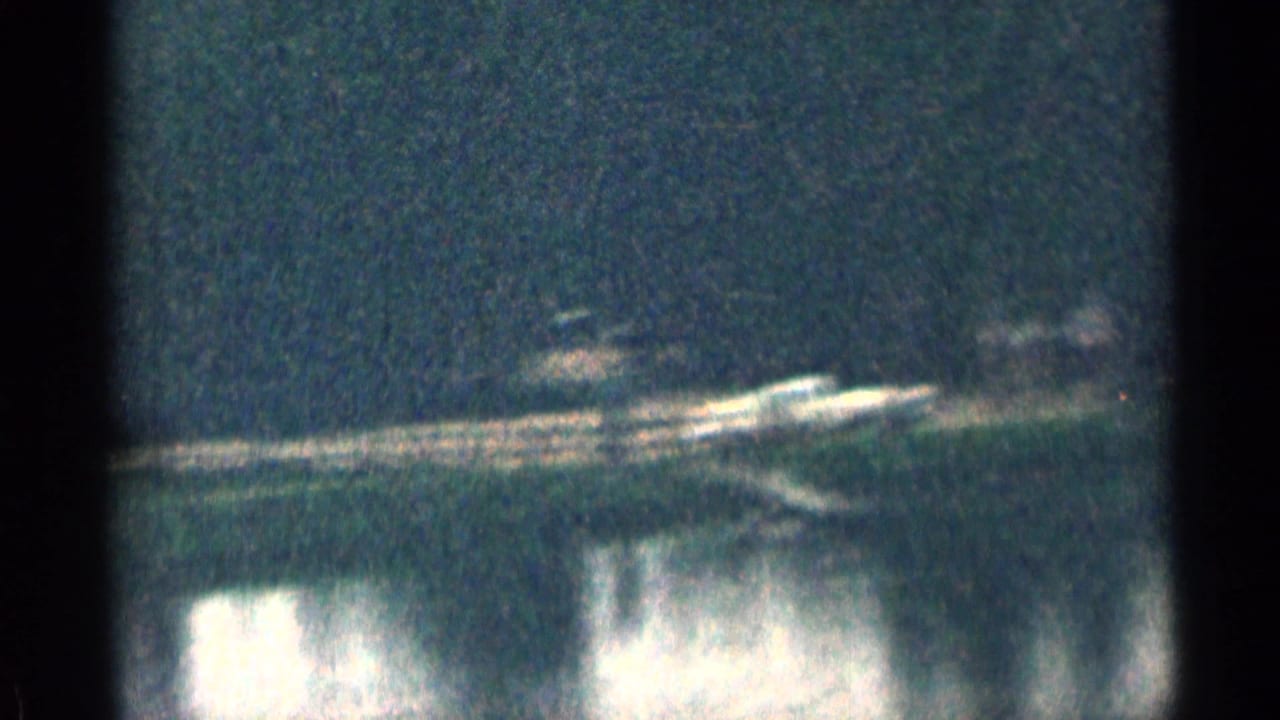 A blue-tinted 8mm frame shows a bright horizontal line of lights or shoreline detail above dark reflective water.