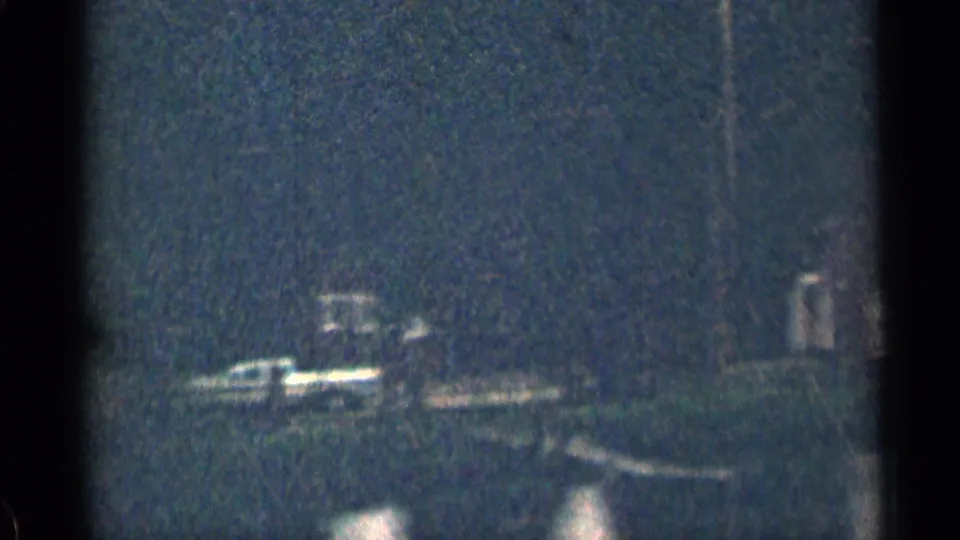 Nighttime 8mm frame from Colorado showing bright blurred forms near a dark road or shoreline with reflected light below.