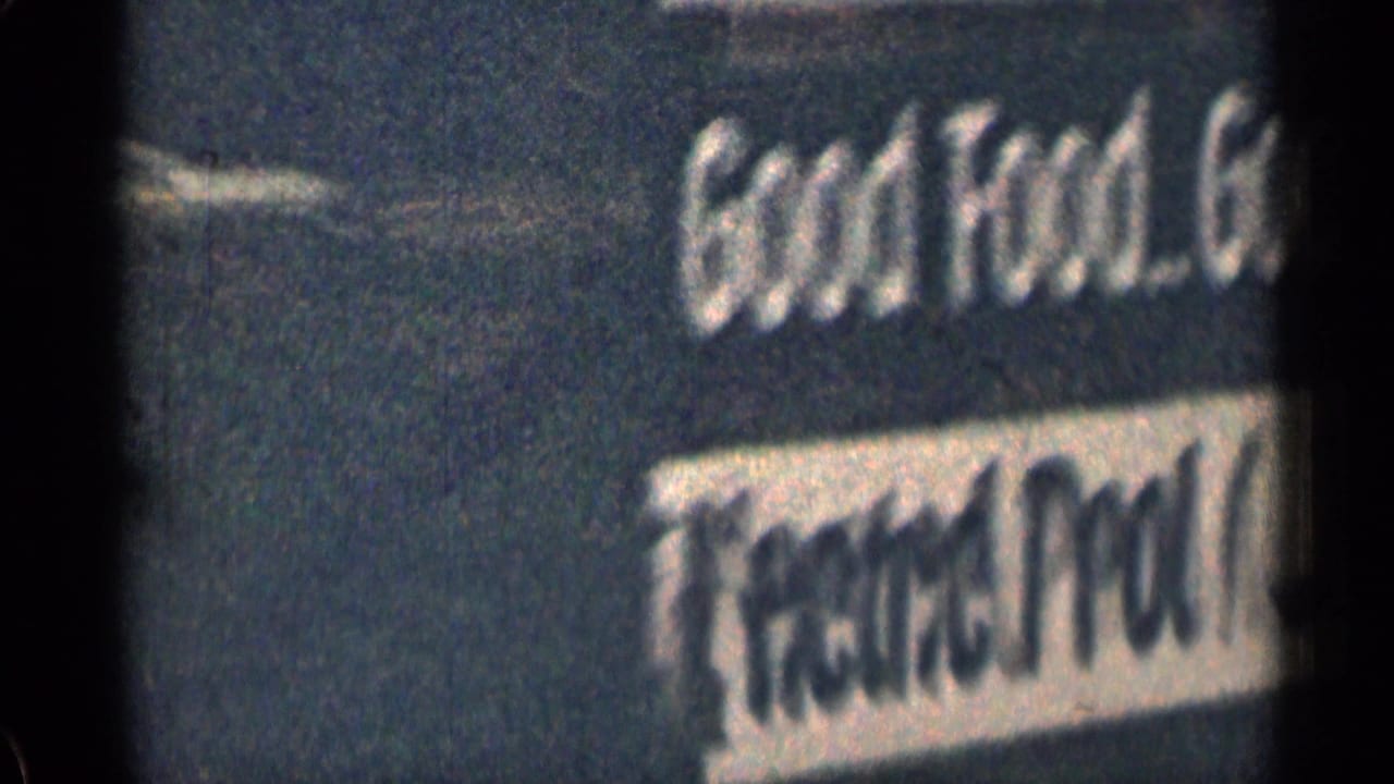 Blurred roadside motel or lodge sign in 1963 Colorado footage, showing Good Food and Overnight Guest lettering.