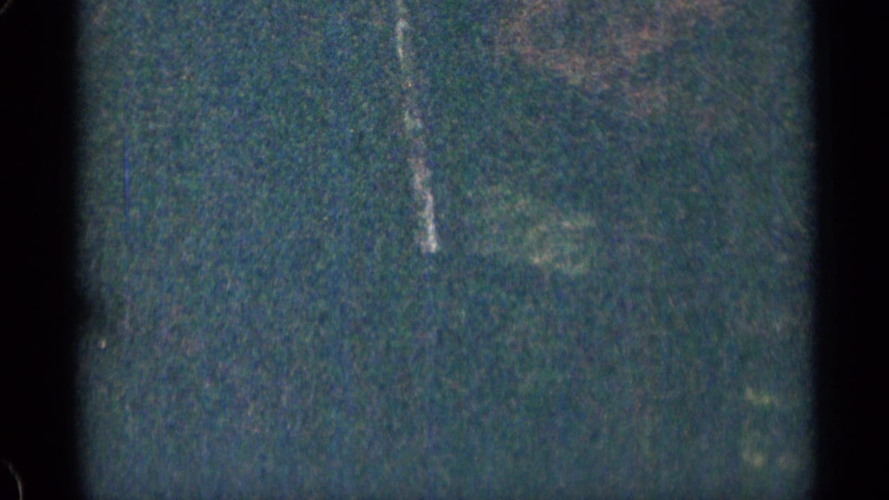 Dark, blurred roadside view through the car window with faint trees or structures.