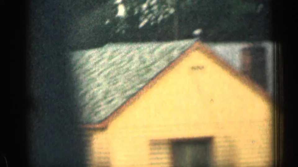 1963 Colorado 8mm view of a yellow roadside cabin or lodge building with a sloped roof, framed by trees and car-window edges.