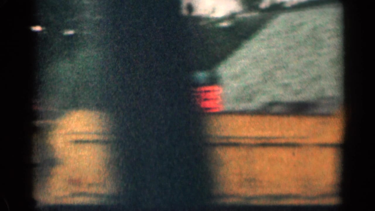 1963 Colorado 8mm frame with a dark car passing or parked near a roadside sign and low commercial building.