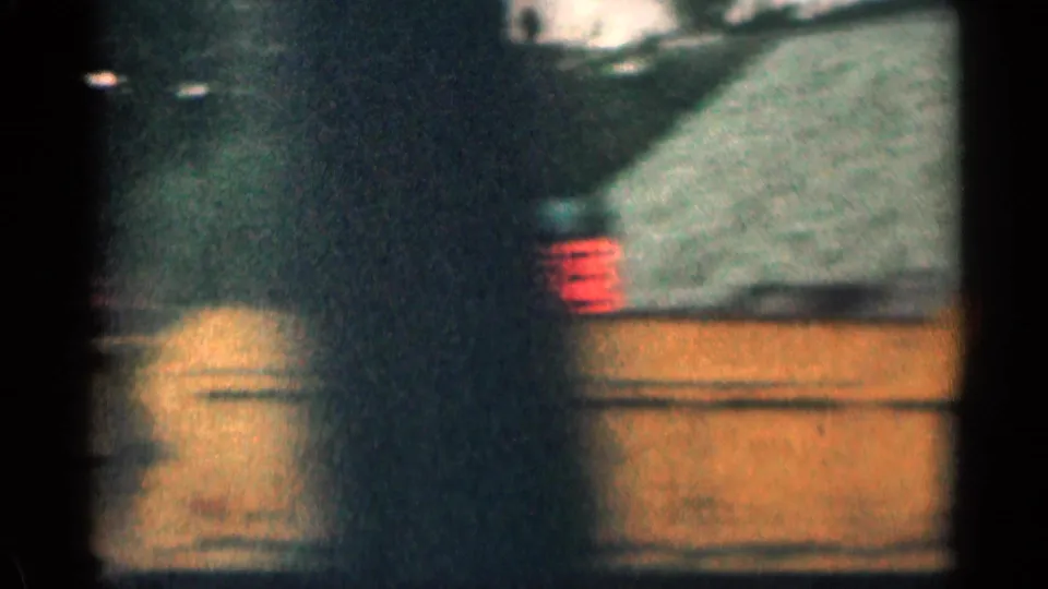 1963 Colorado 8mm frame with a dark car passing or parked near a roadside sign and low commercial building.