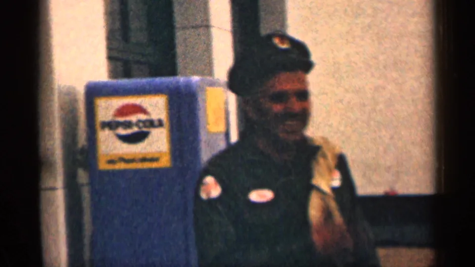 1963 Colorado 8mm frame of a smiling uniformed man in a cap beside a blue Pepsi-Cola vending machine outside a building.