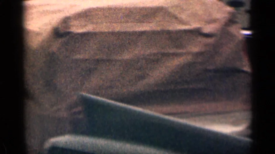The home-movie camera records a blurred roadside or ground surface, with dark framing suggesting a view from inside or past a vehicle.