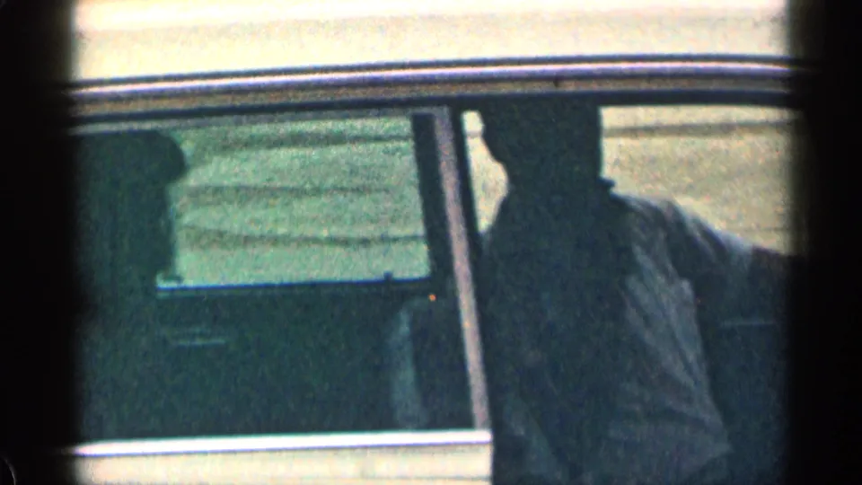 1963 Colorado home-movie frame with two occupants visible as silhouettes through the side windows of a classic American car.
