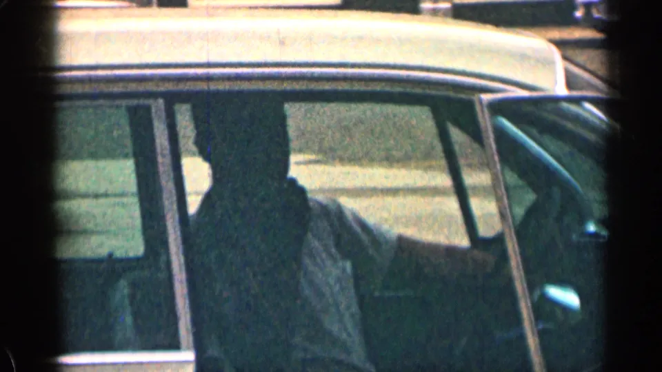 1963 Colorado frame showing a seated car passenger in silhouette, with the vehicle roofline, window frame, and trim clearly visible.